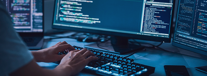 Programista backendowy wykonujący refaktoryzację kodu na wielu monitorach w nowoczesnym technologicznie miejscu pracy