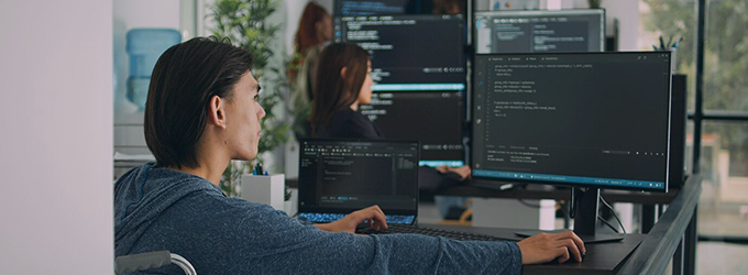 Developer collaborating with team, reviewing code on multiple monitors in a bright office