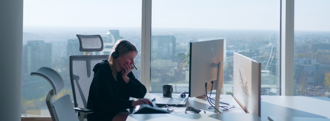 A developer in a headset working on a digital product, deep in thought, with a city view behind.