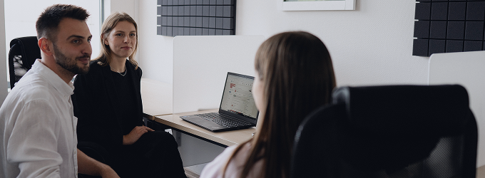 Trzech kolegów siedzących przy laptopie, zaangażowanych w dyskusję na temat projektu w nowoczesnym miejscu pracy