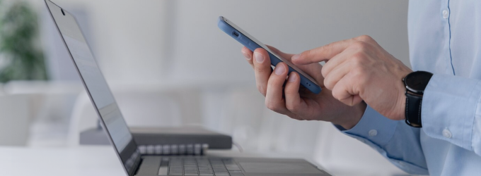 Ingegnere QA che convalida la funzionalità dell'applicazione mobile sul telefono, con il codice del laptop visibile sullo sfondo