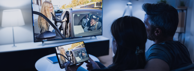 Um casal assiste a um filme sincronizado entre o tablet e a televisão, mostrando a transmissão de vídeo multiplataforma em ação.