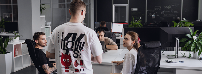 Group of coworkers gathered at a workstation during a daily stand-up meeting in a creative office space.