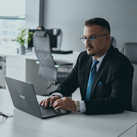 Empleado de oficina sentado en un escritorio, tecleando en un portátil durante un trabajo concentrado en un entorno de trabajo contemporáneo.