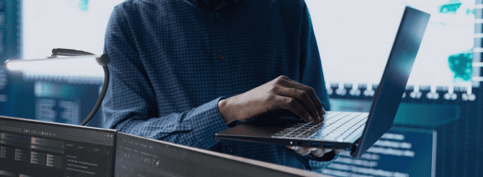 Software engineer configuring applications on a laptop surrounded by server monitors in a modern tech workspace