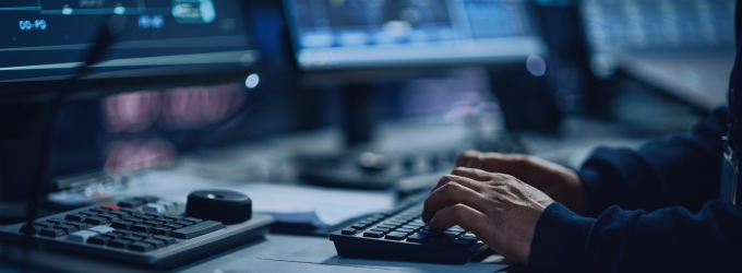 Sviluppatore che scrive codice su una tastiera, circondato da schermi multipli con interfacce software