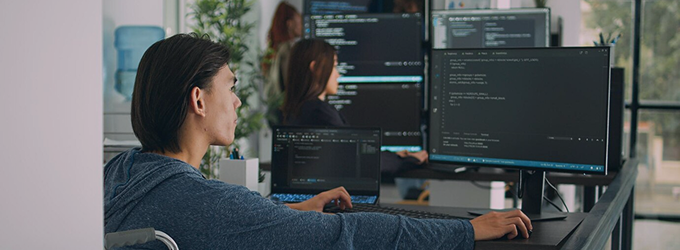 Deweloper współpracujący z zespołem, przeglądający kod na wielu monitorach w jasnym biurze