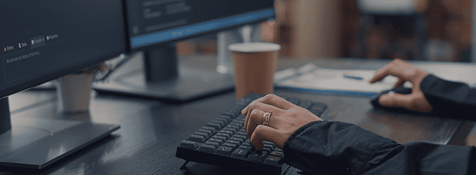 Software developer coding at a dual-monitor workstation in a modern office environment
