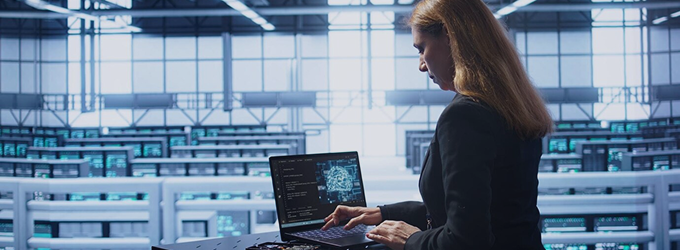 Tech professional coding AI applications on a laptop, standing among server racks in a high-tech facility
