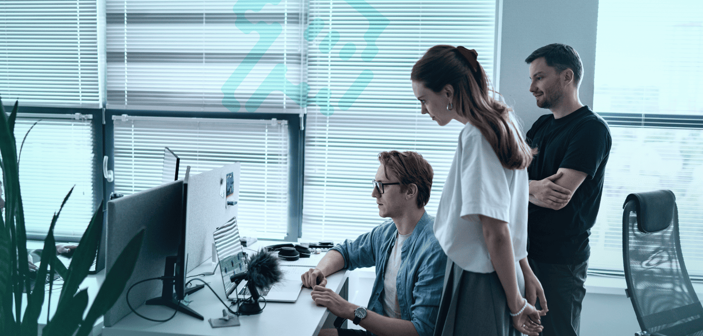 Team members gathered around a desk, debugging a software issue in front of a screen in a naturally lit office