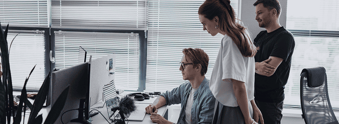 Team members gathered around a desk, debugging a software issue in front of a screen in a naturally lit office