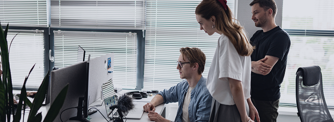 Team members gathered around a desk, debugging a software issue in front of a screen in a naturally lit office.
